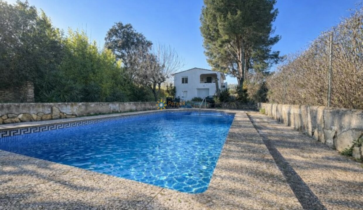 Piscina al sol con casa blanca